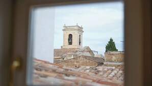 A view through a window of a building with a bell tower, tiled roofs, and a green tree. - Hotel Maia Menorca (Ciutadella de Menorca)
