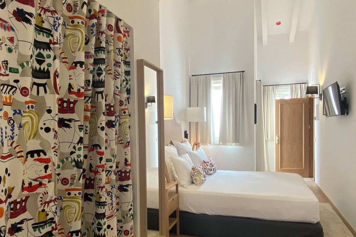 Un dormitorio con cama, espejo, mesita de noche, lámpara y armario.
