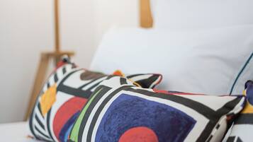 Ein Bett mit bunten Kissen und einer Lampe auf einem weißen Nachttisch.