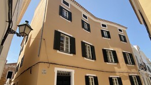 A building with a beige facade, black shutters, and a tiled ground. - Hotel Maia Menorca (Ciutadella de Menorca)