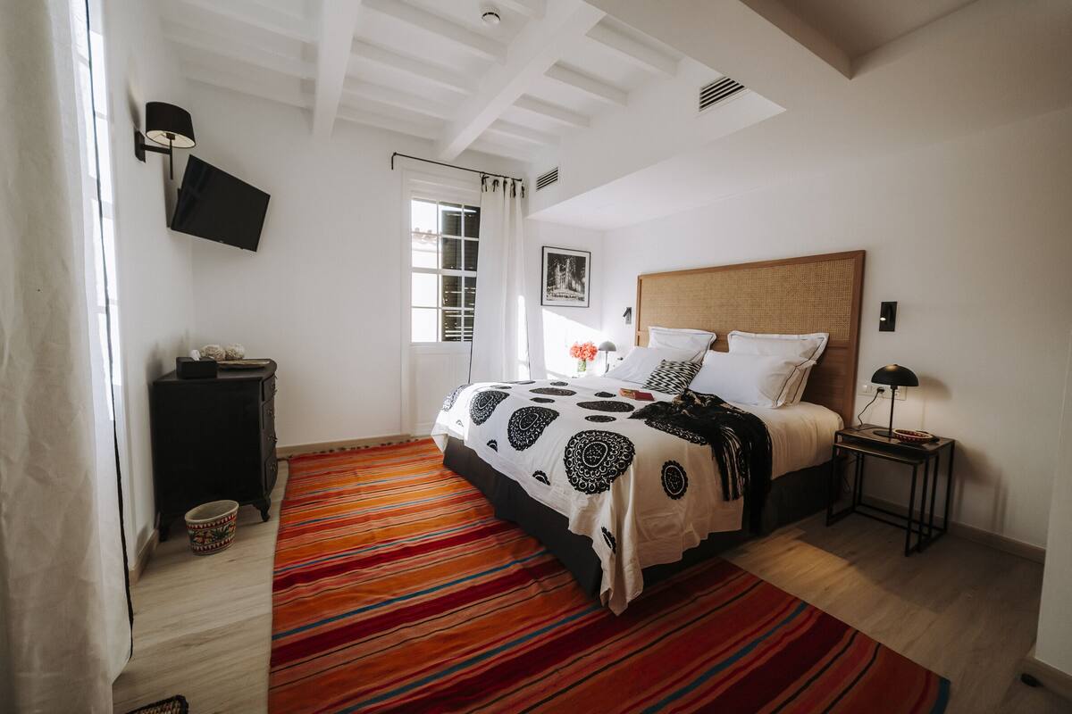 A bedroom with a bed, a nightstand, a TV, and a window with curtains.