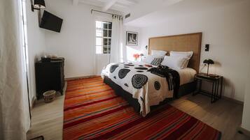 A bedroom with a bed, a nightstand, a TV, and a window with curtains.