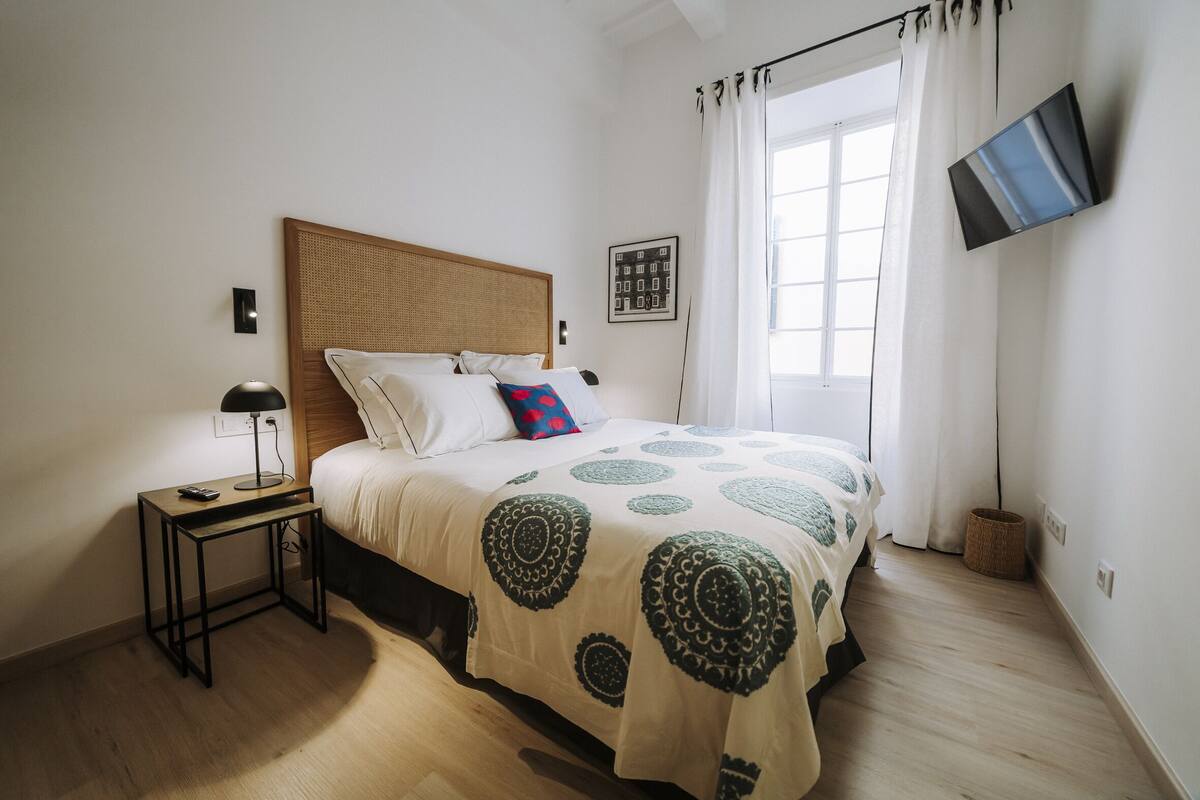 A bedroom with a bed, bedside table, lamp, and a TV mounted on the wall.