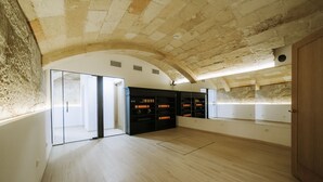 A spacious room with a high ceiling, stone walls, and a wooden floor. There are built-in shelves with storage boxes and a large window providing natural light.