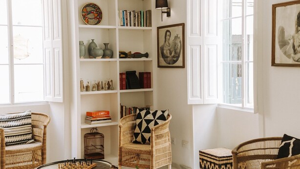 A cozy living room with a bookshelf, wicker furniture, and a striped rug.