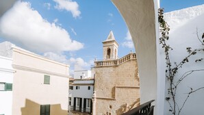 A balcony with a view of a historic building with a bell tower, a white wall with a plant, and a tiled floor.