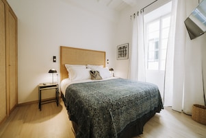 Une chambre à coucher avec un lit, des tables de chevet, un téléviseur fixé au mur et une fenêtre avec des rideaux.