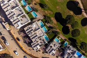 Eine Vogelperspektive eines Hotels mit mehreren Gebäuden, einem Schwimmbecken und umliegender Bepflanzung.