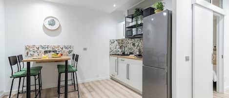 A modern kitchen with a large refrigerator, a dining table with chairs, and a microwave shelf.