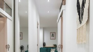 A modern hallway with a wooden floor, a green sofa, and a wall-mounted macrame piece.