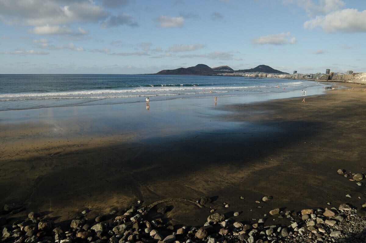 A beach with clear water, pebbles, and distant mountains.