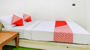 Ein Einzelbett mit weißer Matratze und rot-weißer Bettwäsche. Neben dem Bett steht ein kleiner Holztisch.