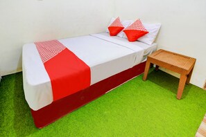 Ein Einzelbett mit einer rot-weißen Tagesdecke, zwei rote Kissen und ein kleiner Korbtisch.