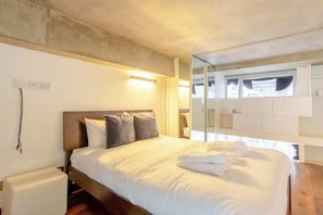 A modern hotel room with a large bed, bedside lamps, a wardrobe, and a view through a window.