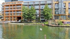A modern apartment building with balconies, a canal in front, and a swan in the water. - Incredible 2BD Loft by Regents Canal - Haggerston (London)