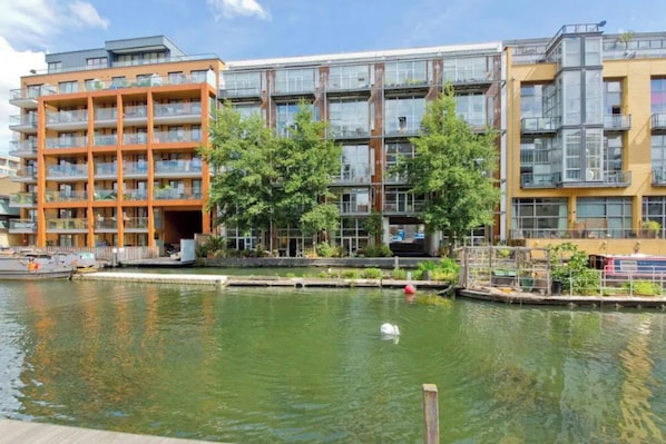 A modern apartment building with balconies, a canal in front, and a swan in the water.