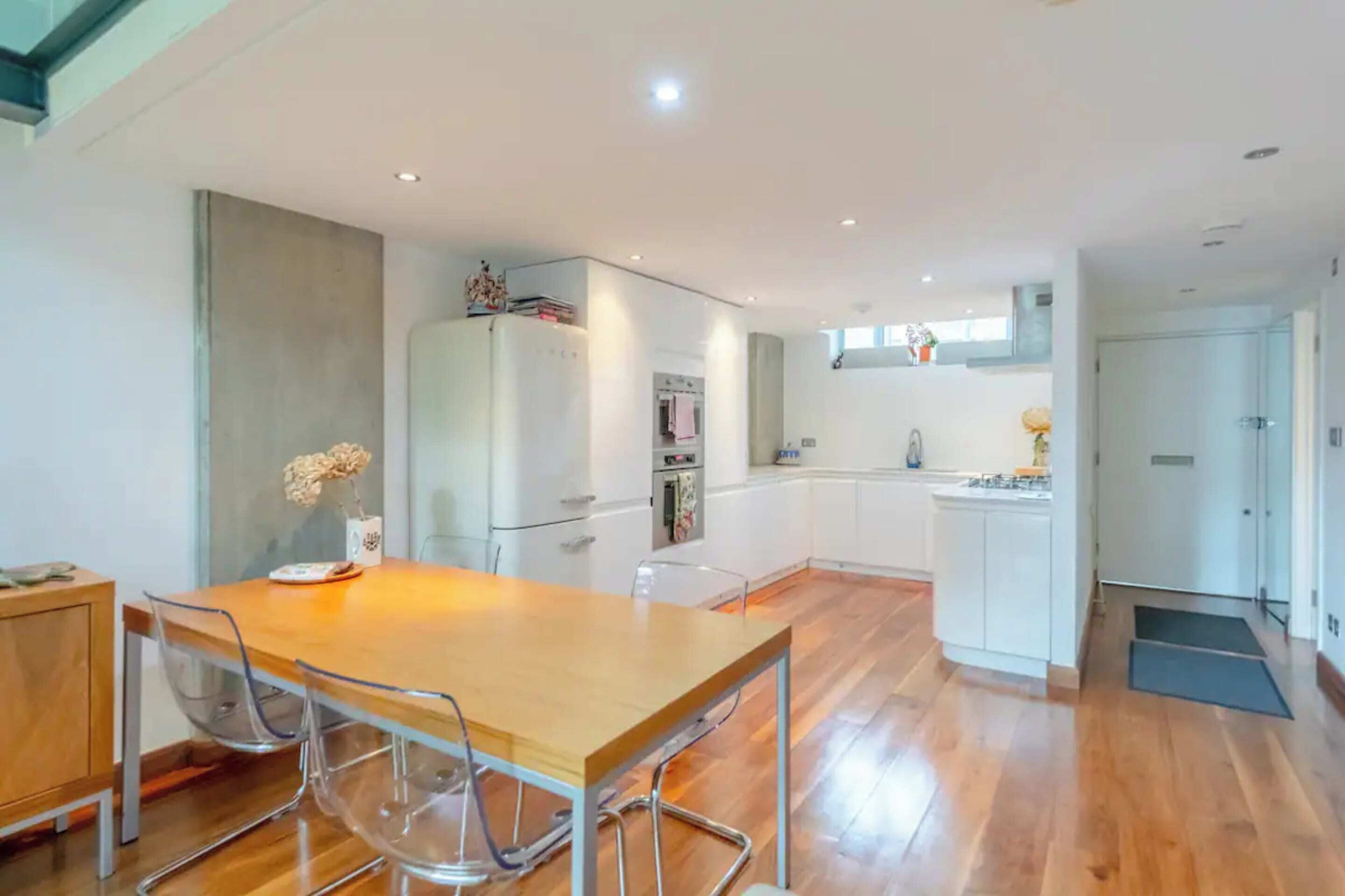 A modern kitchen with white cabinets, a wooden dining table, and clear chairs.
