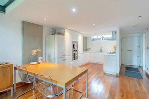 A modern kitchen with white cabinets, a wooden dining table, and clear chairs.