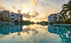 Ein ruhiger Hotelpool mit klaren Spiegelungen der Gebäude und Palmen, umgeben von üppiger Vegetation.