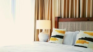 Een hotelkamer met een groot bed, beige gordijnen, een houten hoofdeinde en een bedlamp.