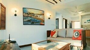 Een woonkamer met een bank, een salontafel en een schilderij van boten aan de muur.