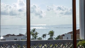 Uitzicht vanaf een balkon met houten frame, uitkijkend over een kustgebied met palmbomen en een gebouw met pannendak.