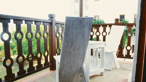 Een balkon met een houten stoel en een witte tafel, omgeven door een sierhekwerk.