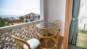 Uma varanda com mesa redonda e cadeiras, vista para o mar e um edifício ao fundo.