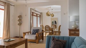 A living room with a sofa, armchair, wooden coffee table, and a dining area with chairs and a table. - The Sultan Palace Beach Retreat Three-Bedroom Villa (Kikambala, Mombasa)
