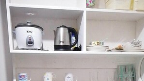 Une cuisine dotée d’un plan de travail en granit, d’un évier en acier inoxydable et de meubles en bois. On y trouve deux appareils : une mijoteuse blanche et une bouilloire électrique noire. Le plan de travail contient également quelques tasses et un petit récipient.