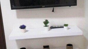Un téléviseur à écran plat fixé au mur, avec trois étagères blanches en dessous.