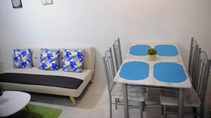 Un salon comprenant un canapé, une table à manger avec des sets de table bleus et deux œuvres d’art accrochées au mur.