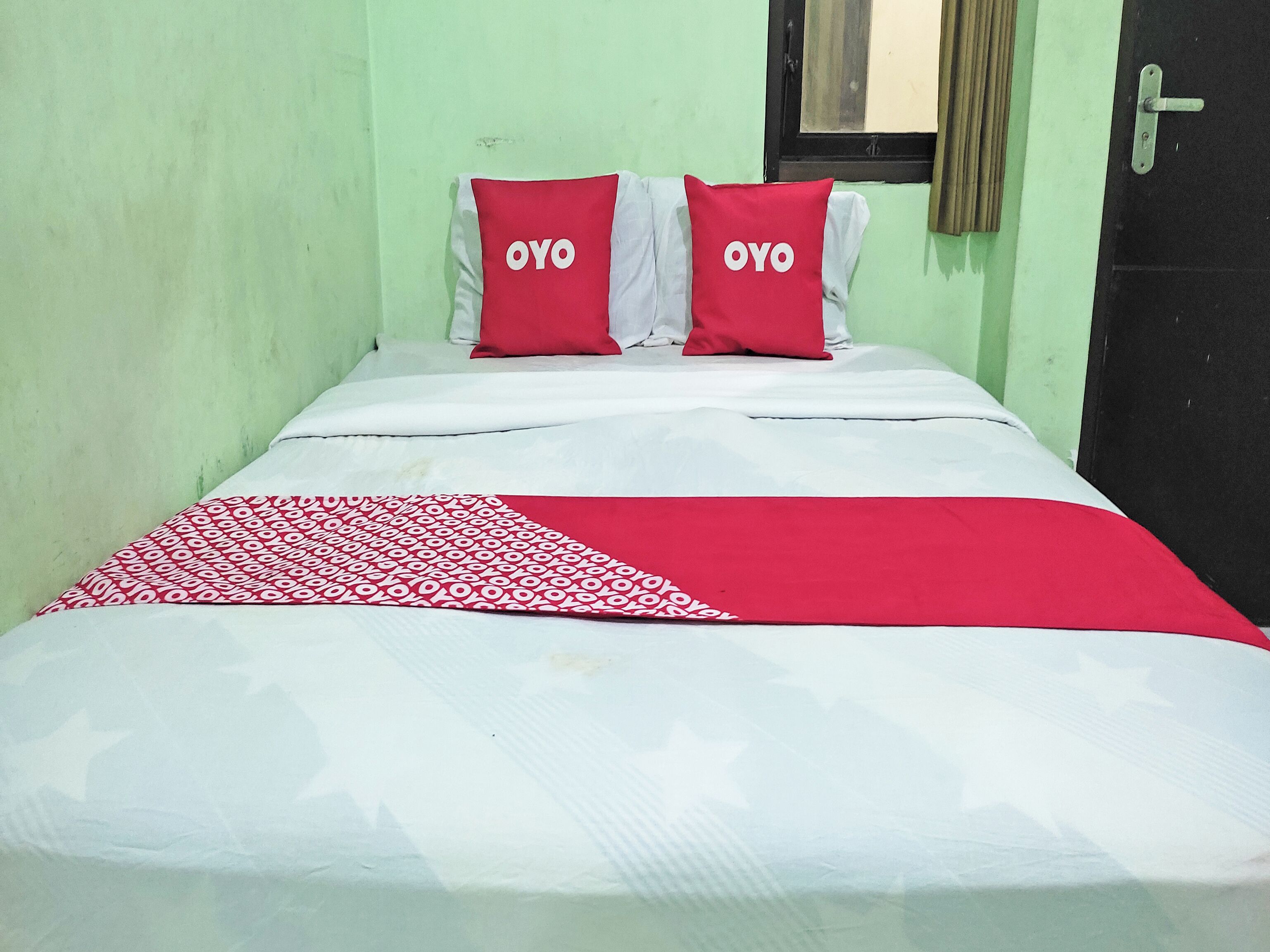 A bed with two red pillows, a white and red blanket, and a green wall.
