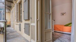 A small, narrow room with a single bed, a window, and a door leading outside.