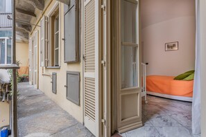 Una habitación pequeña y estrecha con una cama individual, una ventana y una puerta que da al exterior.