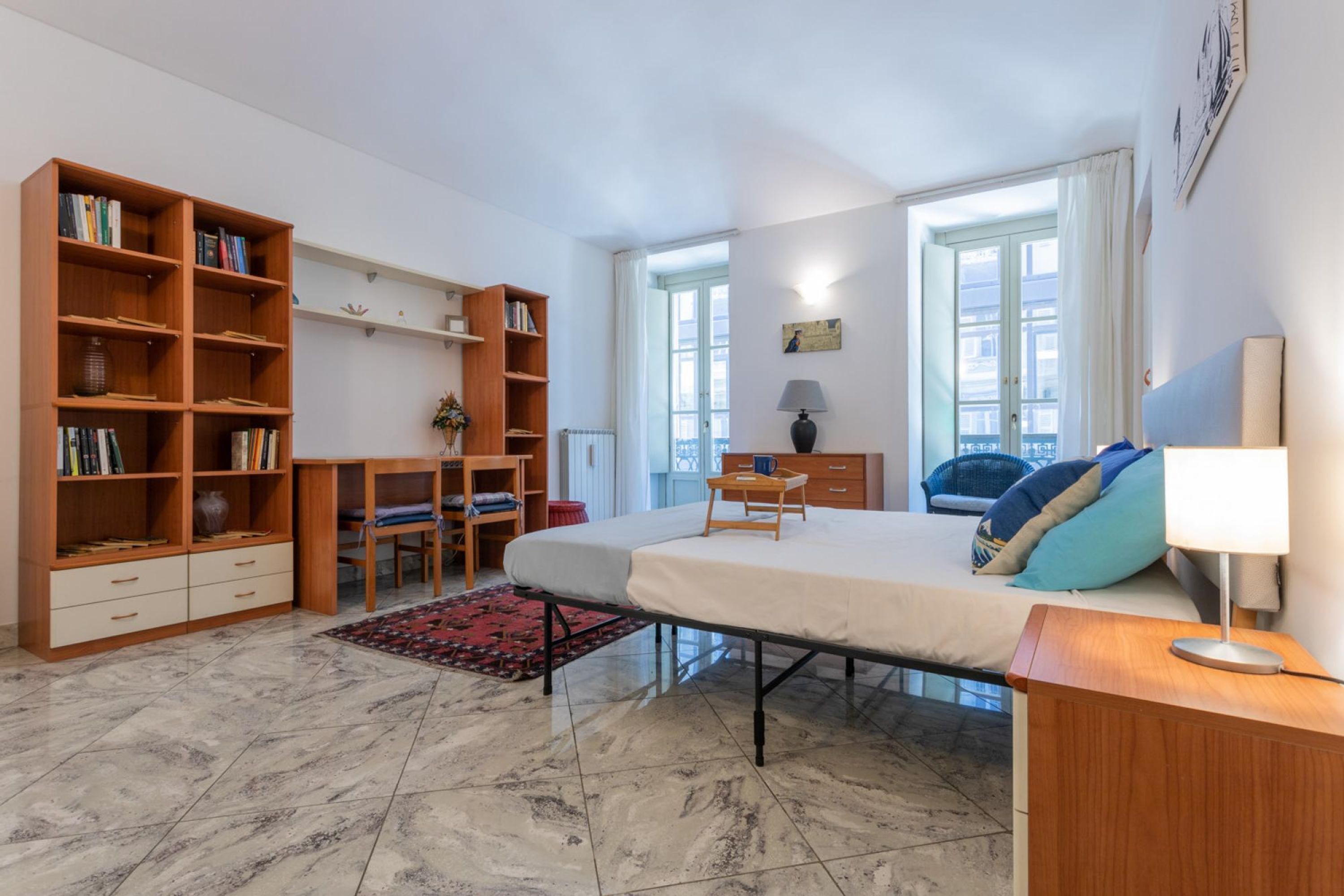 A bedroom with a bed, bedside table, lamp, and a large bookshelf.
