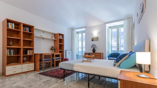 A bedroom with a bed, bedside table, lamp, and a large bookshelf.