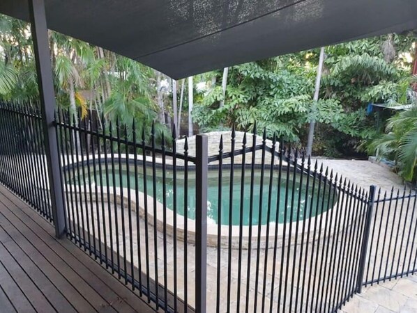 Relax by the serene pool surrounded by lush greenery and a shaded roof structure.