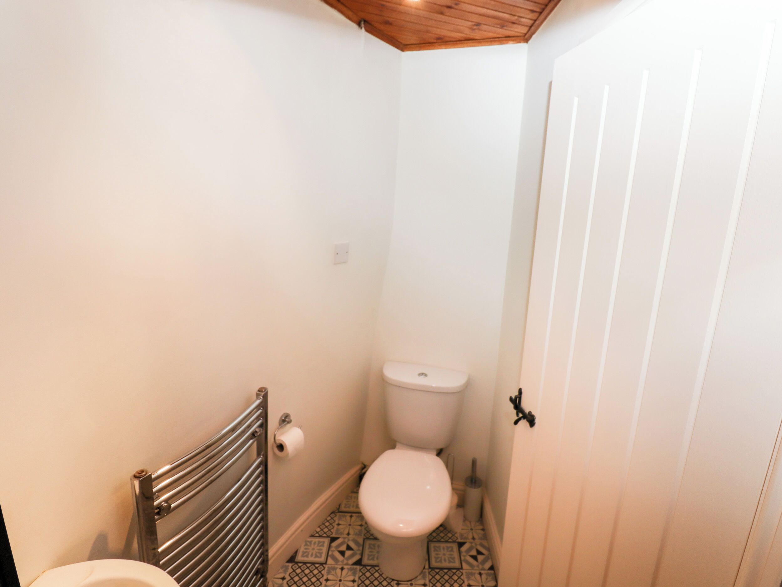 Une petite salle de bain étroite, avec des toilettes, un radiateur en métal et des carreaux de sol à motifs.