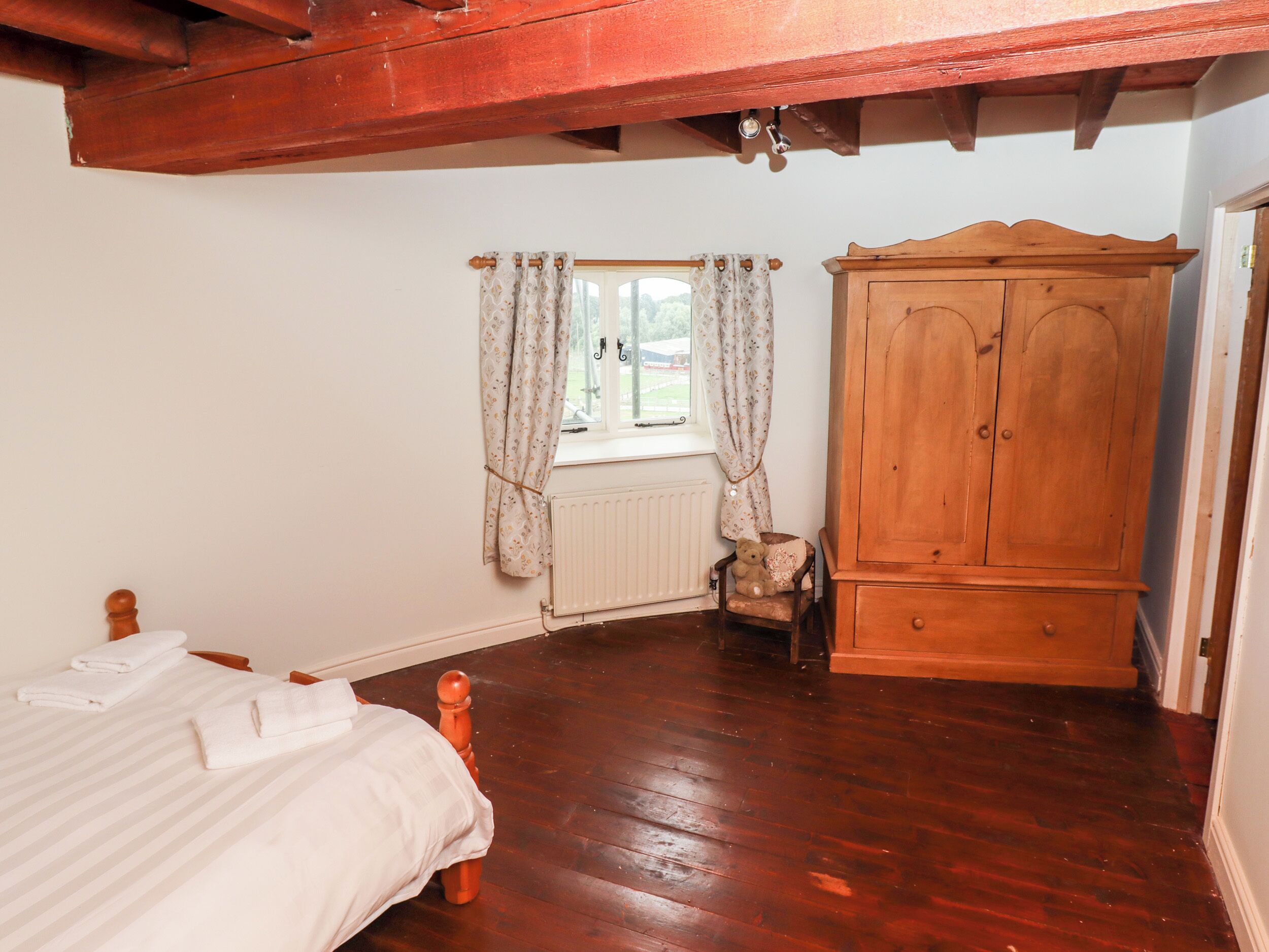 Een slaapkamer met een houten bed, een houten garderobe, een raam met gordijnen en een radiator.