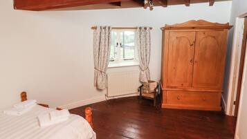 Een slaapkamer met een houten bed, een houten garderobe, een raam met gordijnen en een radiator.