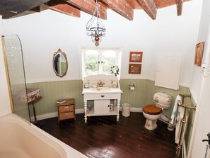 Un baño tradicional con piso de madera, un lavamanos blanco, un espejo, un inodoro y una bañera.