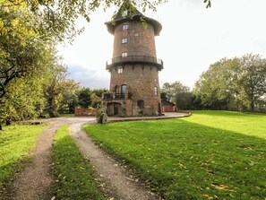 Una torre con fachada de ladrillo y base circular, rodeada de césped y árboles.
