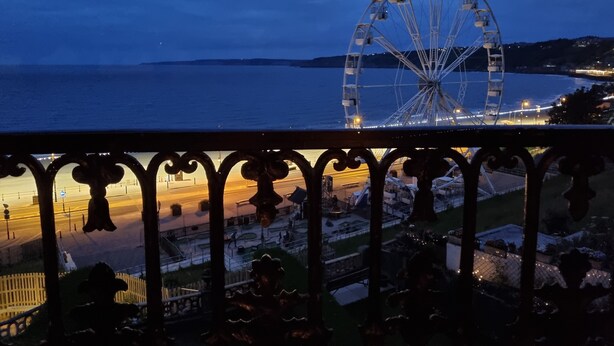 Uma roda gigante ao entardecer, com vista para o mar e o horizonte da cidade ao fundo.