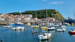 Uma marina com vários barcos atracados, uma colina com edifícios e um céu azul límpido.