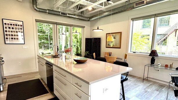 A modern kitchen with a large island, white cabinetry, and a view of the outdoors through large windows. - Luxury Creekside Condo , steps away from shopping & dining (Traverse City)