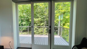 A room with a sliding glass door leading to a balcony with a wooden deck and metal railing. - Luxury Creekside Condo , steps away from shopping & dining (Traverse City)