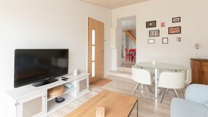 Una sala moderna con un televisor de pantalla plana, una mesa de centro de madera y un comedor con una mesa de vidrio y sillas blancas.