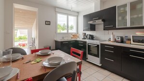 Una cocina moderna con armarios negros, electrodomésticos blancos y un comedor con sillas rojas.