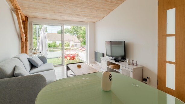 Una sala de estar moderna con sofá, mesa de vidrio, televisor y puerta corrediza de vidrio que da a un espacio exterior.